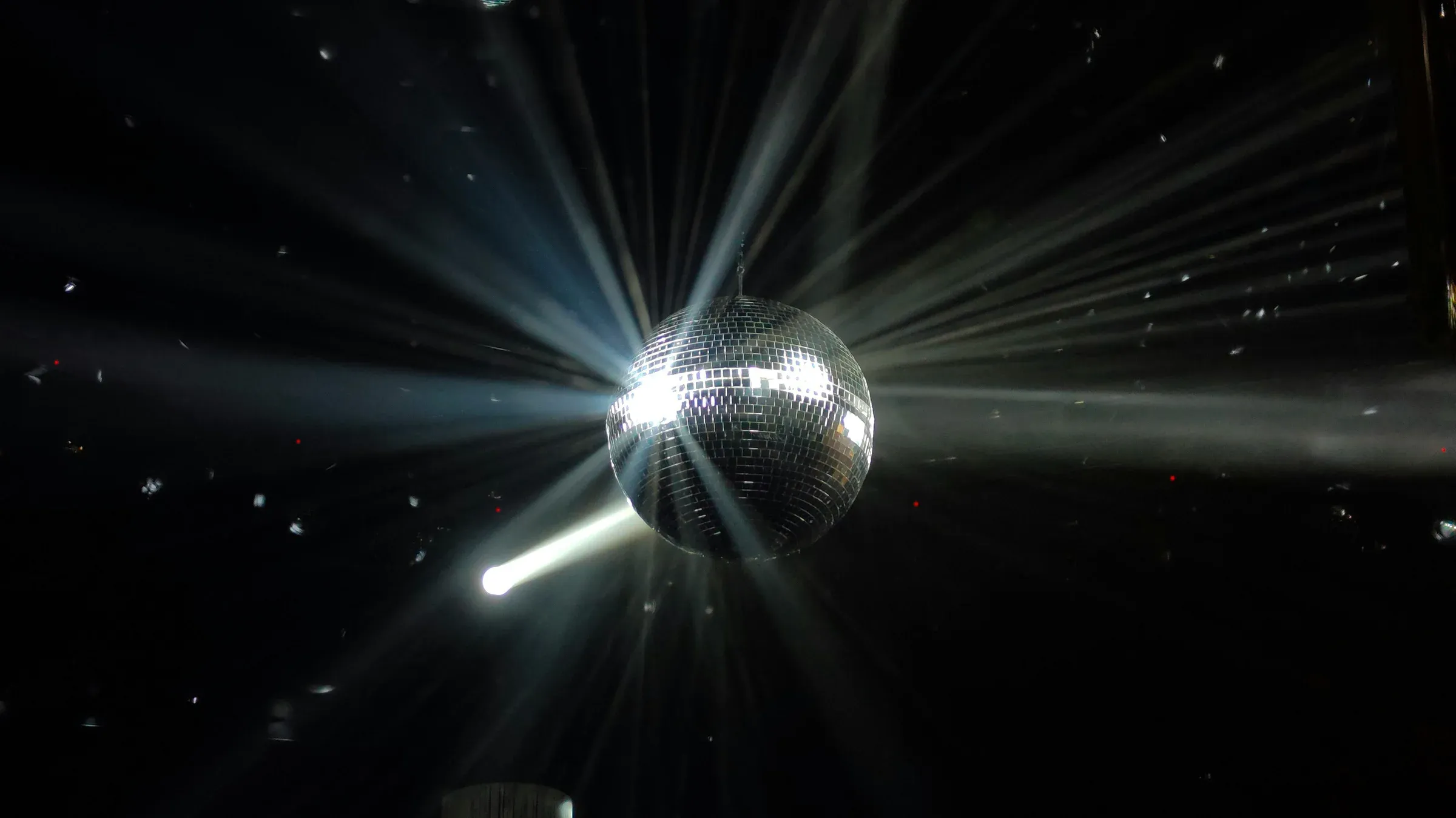Une boule à facettes suspendue dans le noir, éclatée en faisceaux de lumière, des confettis en l'air.