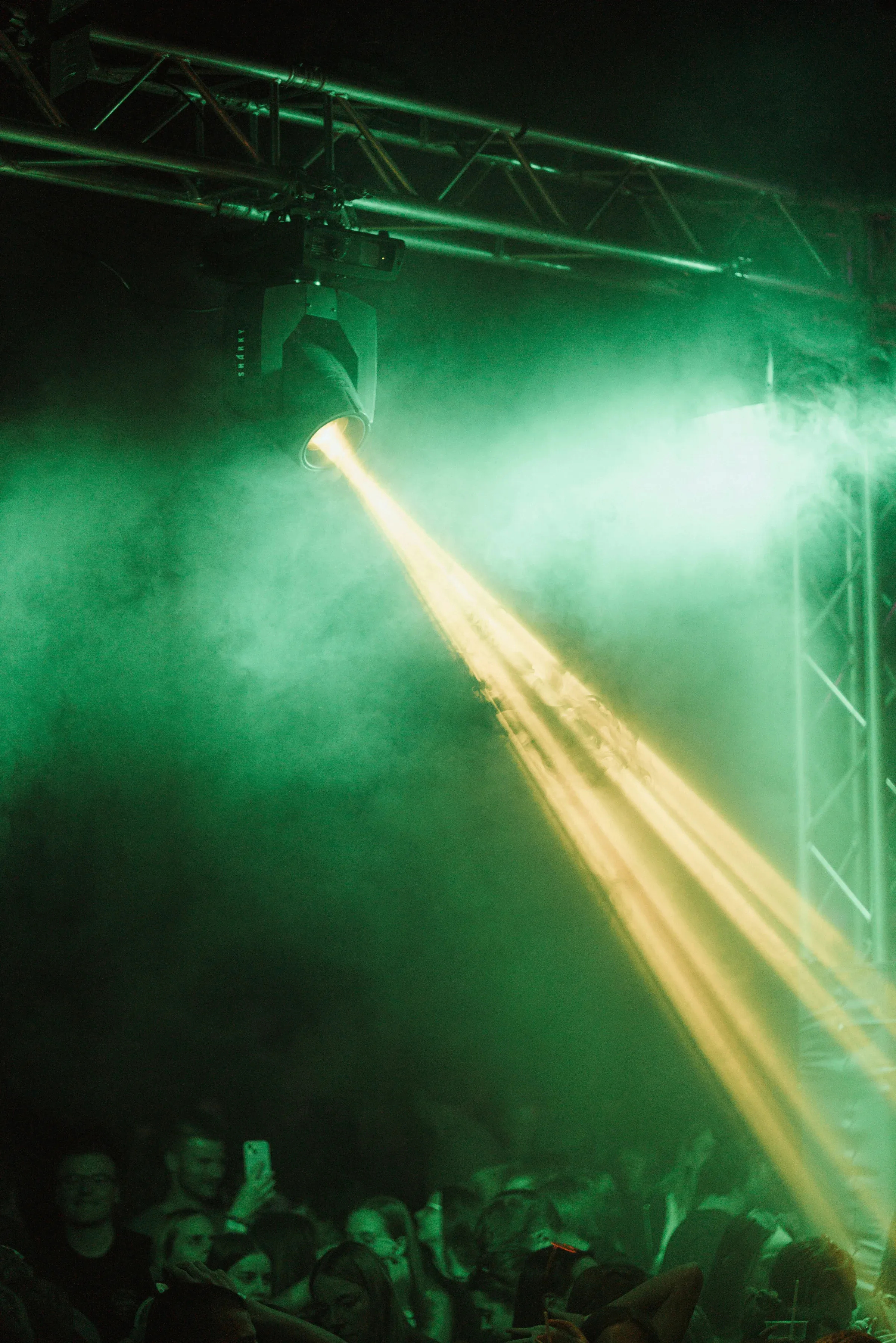 Un projecteur fixé au pont lumière lance un faisceau dans la fumée verte, au-dessus du public.