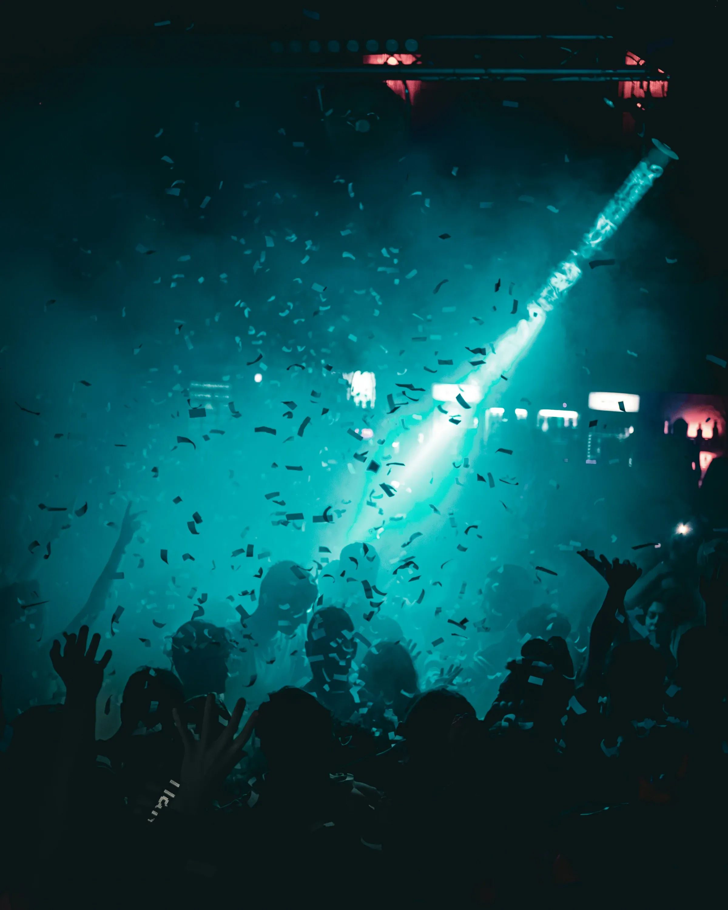 Une foule mains levées sous une pluie de confettis, traversée par un faisceau de lumière.