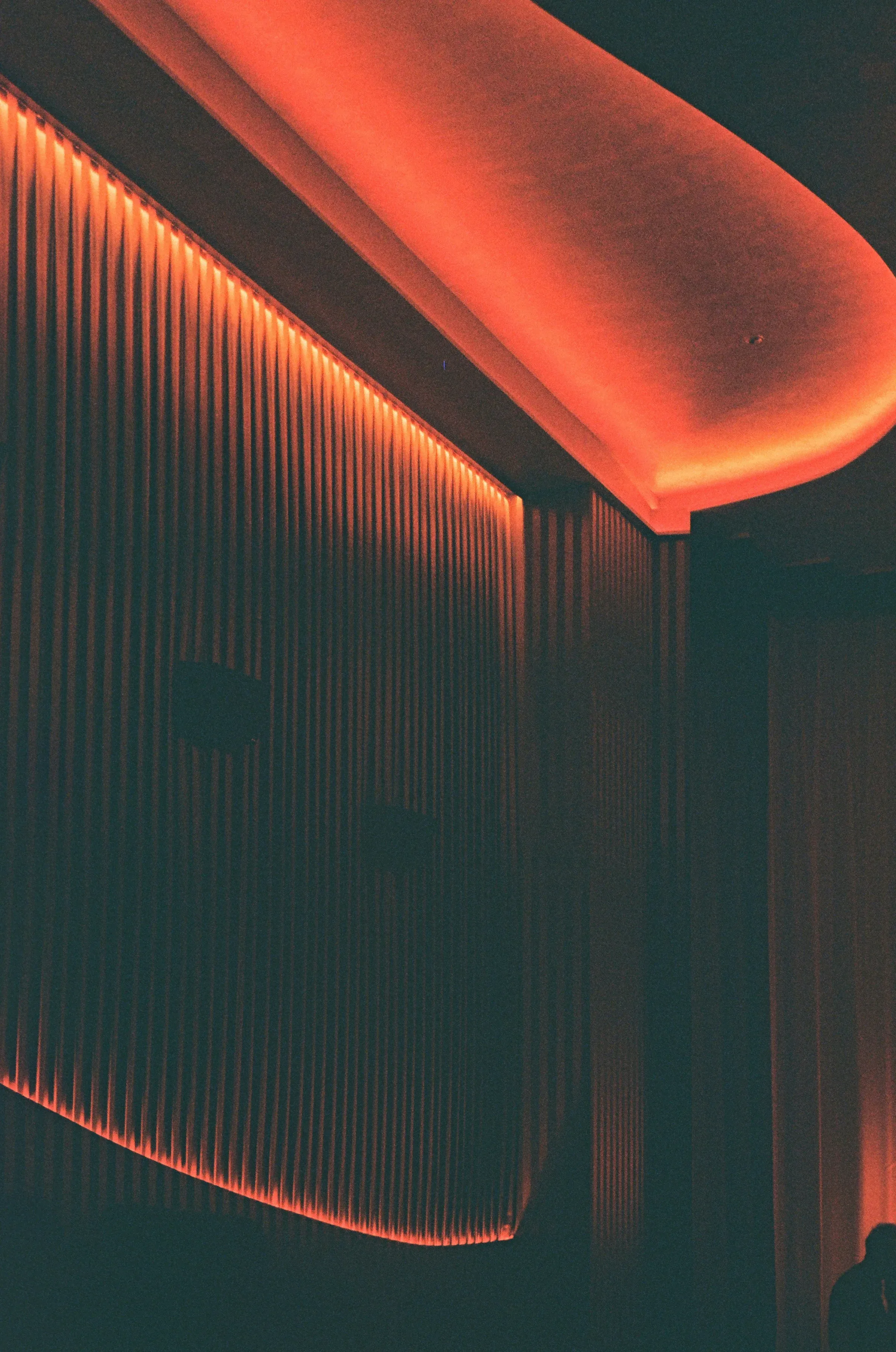 Un plafond en vague et un mur cannelé, soulignés d'un ruban lumineux orangé.