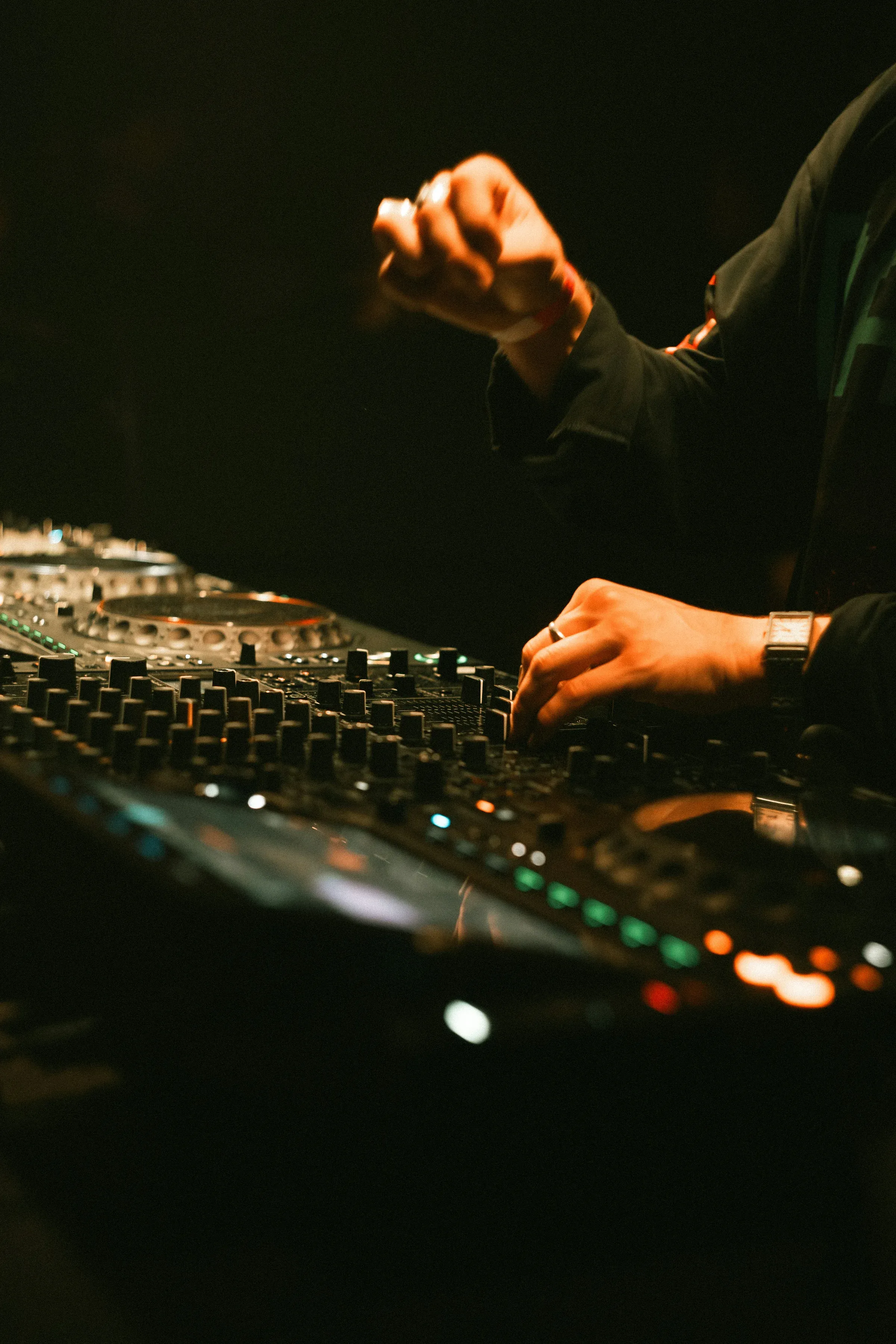 Les mains d'un DJ sur une console de mixage, potentiomètres et platines au premier plan.